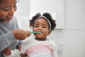 a child having their teeth brushed by their parent